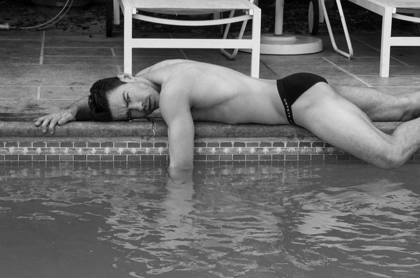 Male model laying poolside in black underwear